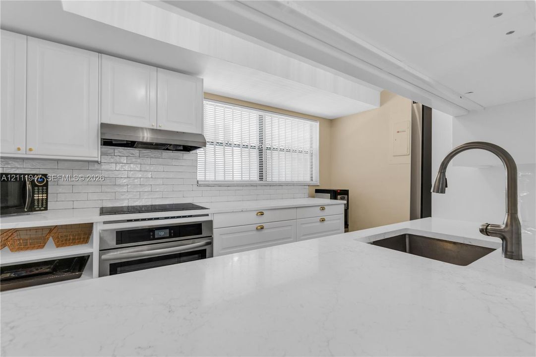 Kitchen featuring white cabinetry, solid-surface countertops, subway tile backsplash, stainless steel appliances, and a gooseneck faucet