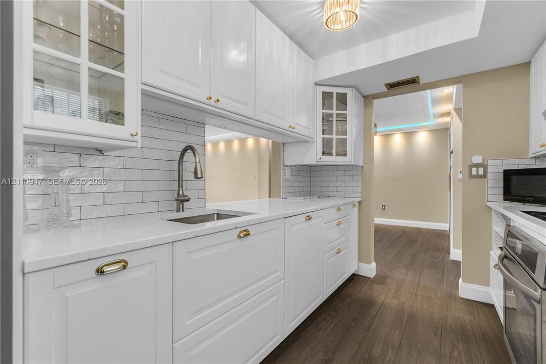 Kitchen featuring white cabinetry with glass-front uppers, white countertops, subway tile backsplash, a gooseneck faucet with undermount sink, and wood-finish flooring