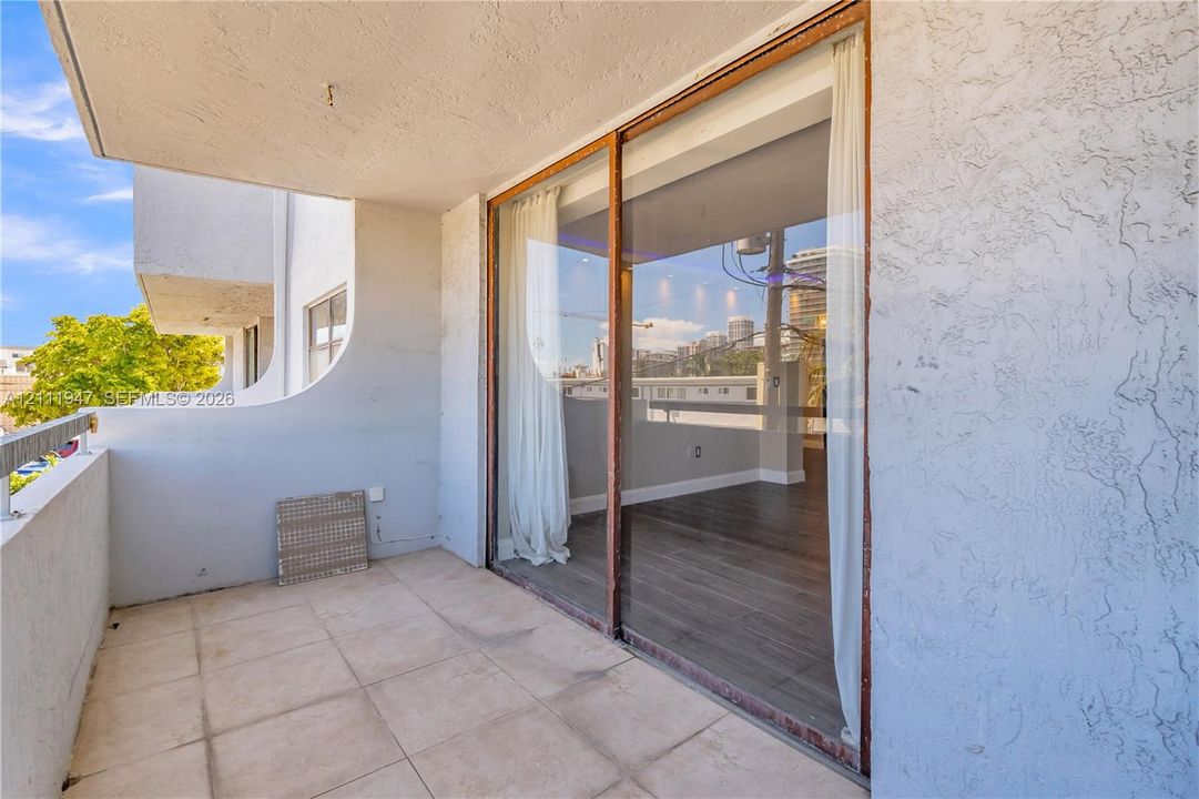 Covered balcony featuring tile flooring, textured stucco walls, and sliding glass doors with wood-finish frames