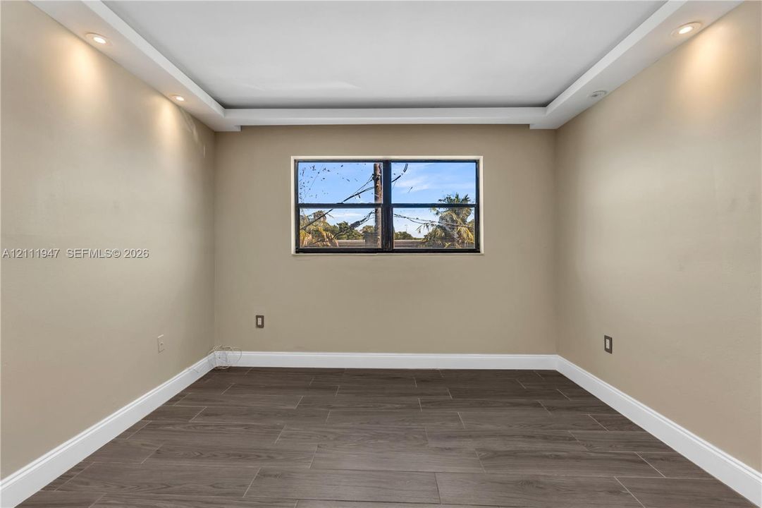 Tray ceiling with recessed lighting, dark wood-finish tile flooring, and a central window with a black frame