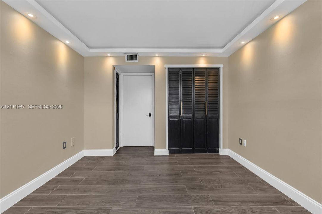 Interior room featuring wood-finish tile flooring, recessed ceiling lighting, a tray ceiling, and dark-toned louvered closet doors