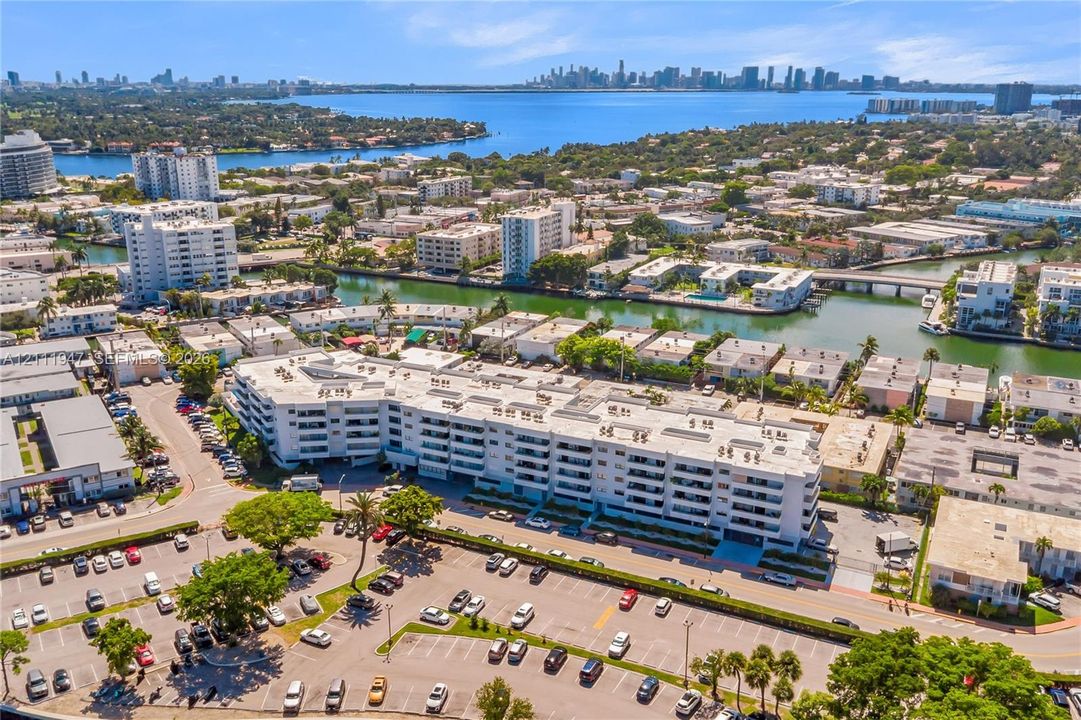 Multi-story building exterior featuring a white facade, private balconies, and proximity to a waterway and coastal skyline