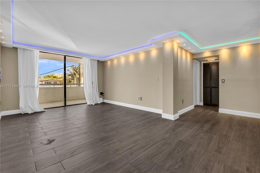 Open-concept room featuring wood-finish flooring, recessed lighting, integrated ceiling accent lighting, and large sliding glass doors opening to a balcony