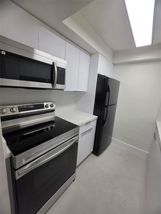 Kitchen featuring white flat-panel cabinetry, light-toned solid surface countertops, stainless steel electric range, over-the-range microwave, and black refrigerator