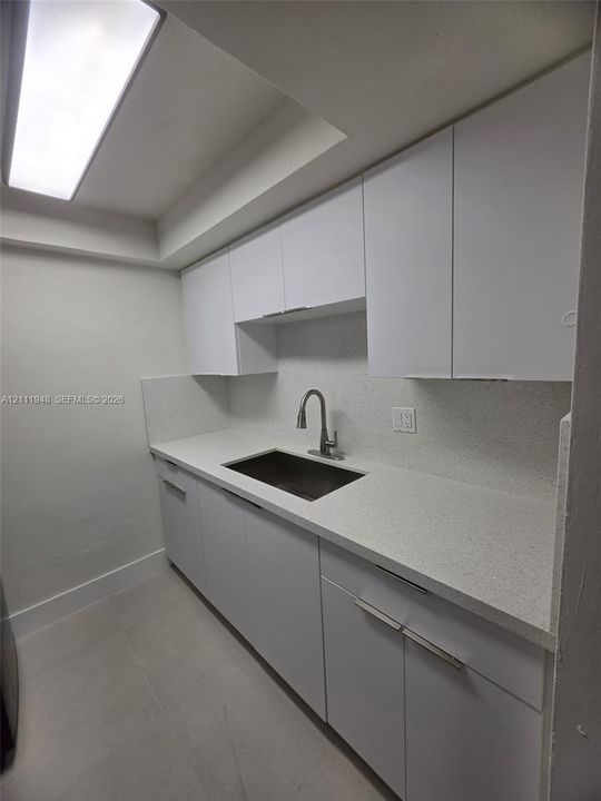 White cabinetry with modern linear hardware, light-toned countertop, undermount sink with gooseneck faucet, and recessed ceiling lighting