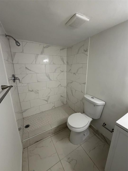 Walk-in shower featuring large-format stone-look wall tiles, hexagonal floor tile, chrome fixtures, and a glass partition, accompanied by a porcelain toilet