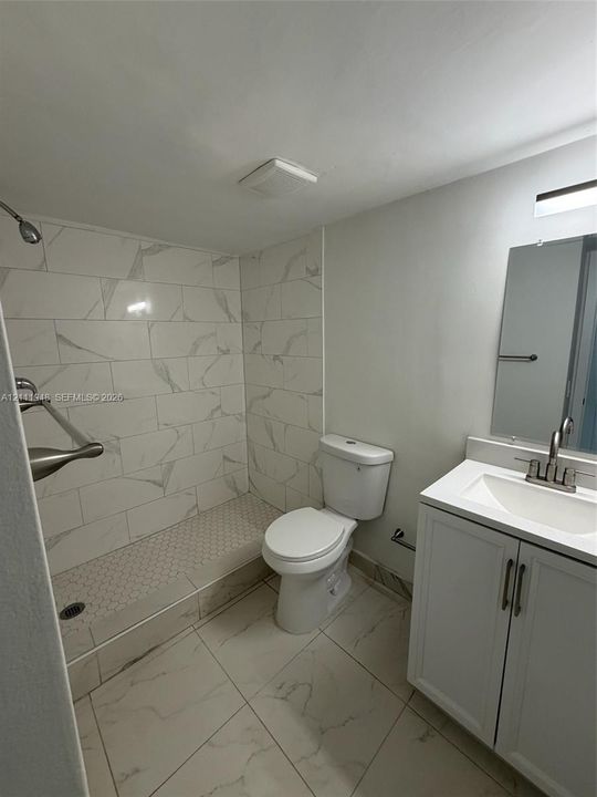 Bathroom featuring large-format veined tile flooring, a walk-in shower with white hexagonal tile flooring and matching wall tile, a white vanity with integrated basin, and a wall-mounted vanity mirror with integrated lighting
