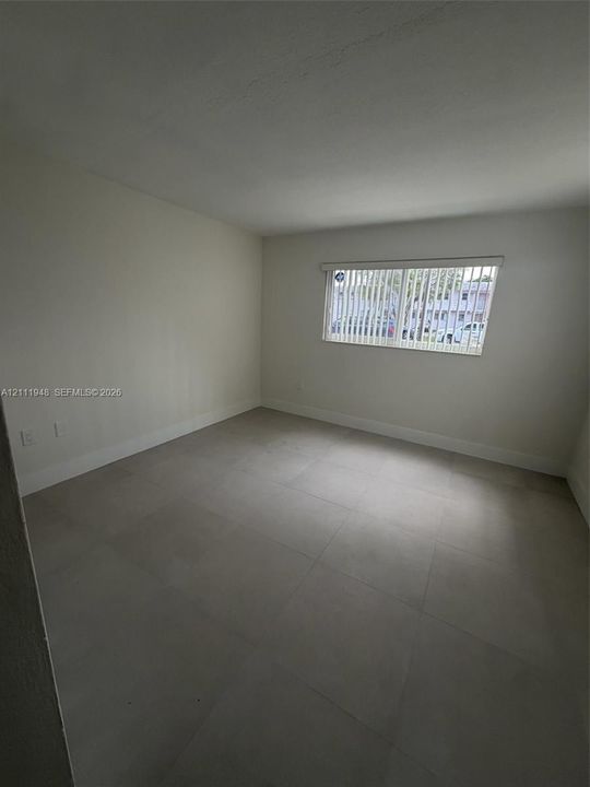Neutral-toned ceramic tile flooring, matte white wall finishes, and vertical window blinds