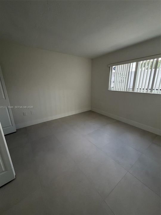 Neutral-toned ceramic tile flooring, solid interior door, and window with vertical blinds