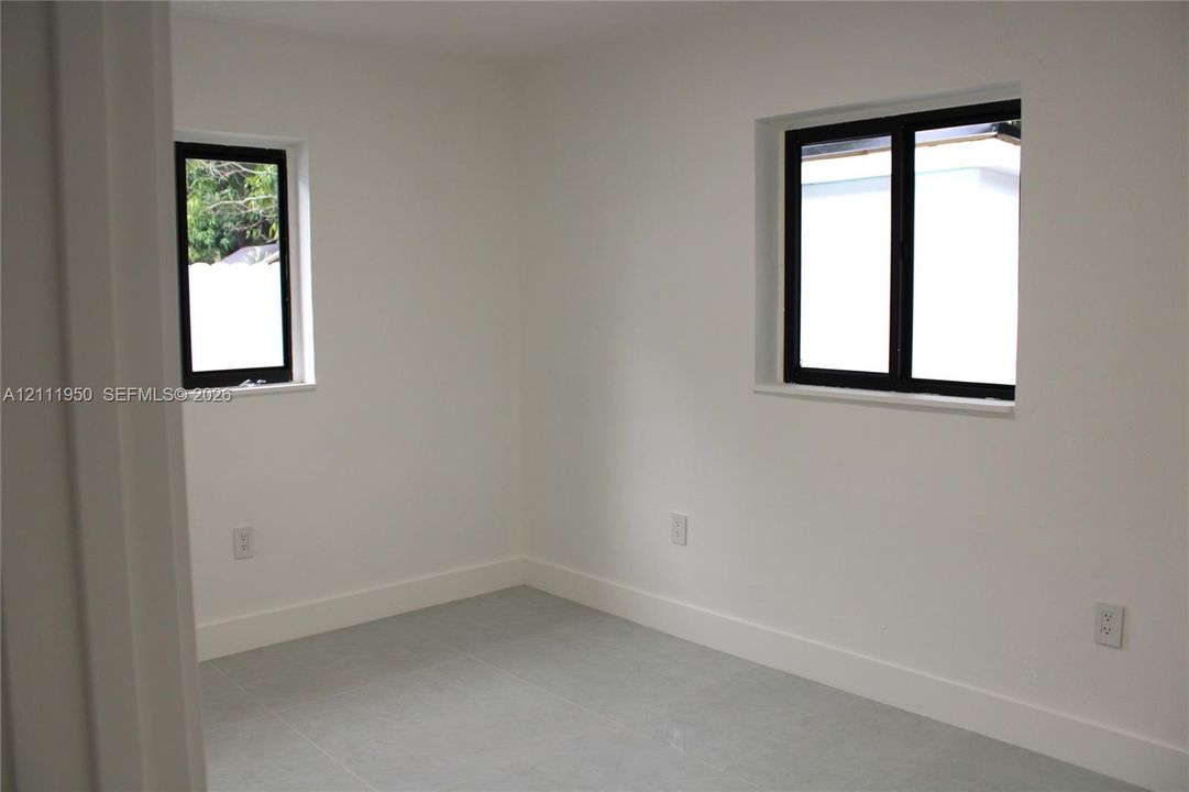 Interior space featuring neutral wall tones, large-format tile flooring, and dual windows with black frames