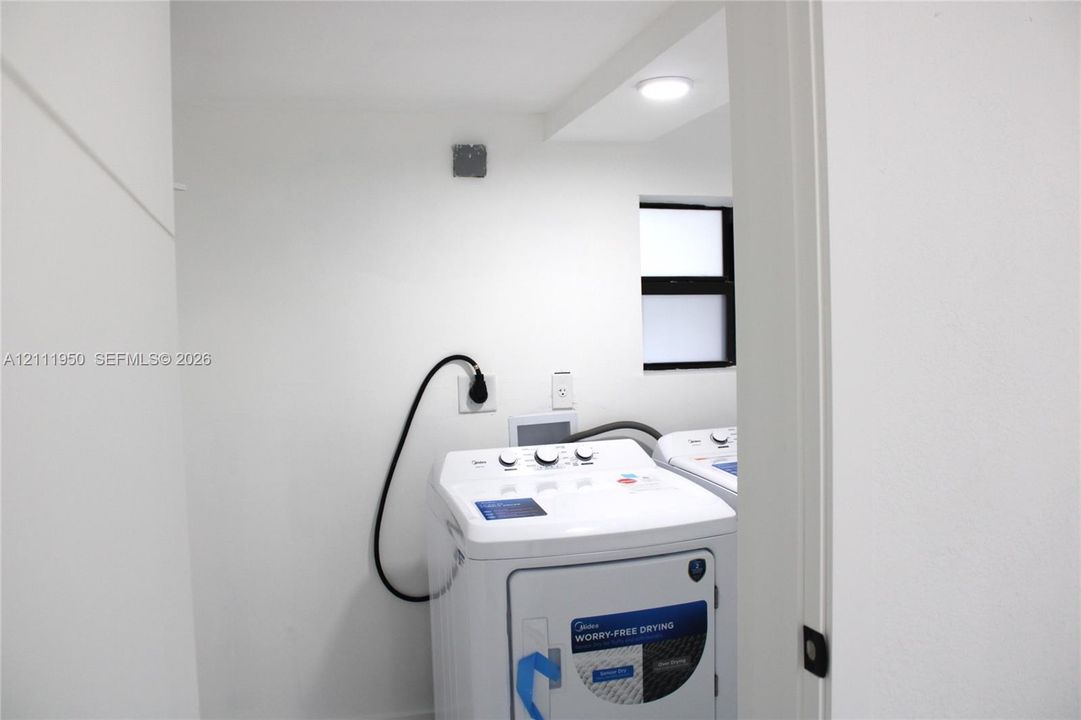 Laundry area featuring high-efficiency top-load washer, dedicated dryer hookups, recessed ceiling lighting, and a window