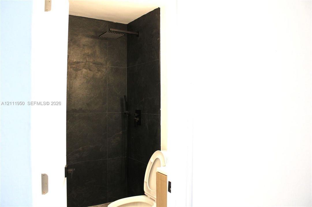 Walk-in shower featuring matte black fixtures, an oversized square rainfall showerhead, and large-format dark stone-finish wall tiles