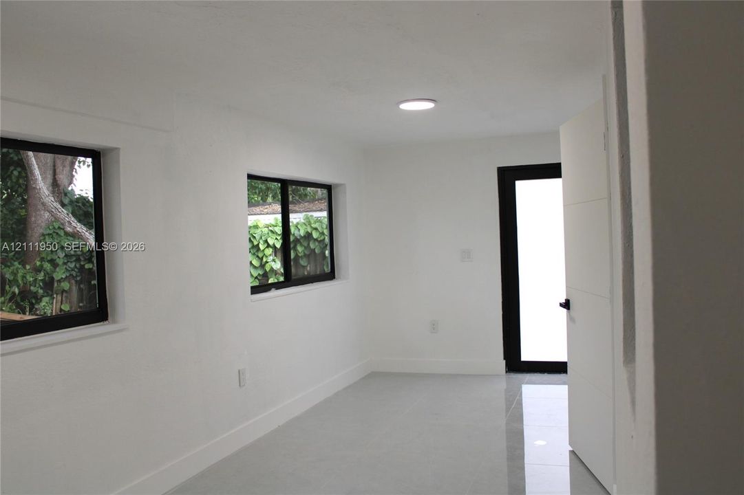 Interior space featuring neutral white walls, large-format tile flooring, recessed ceiling lighting, black-framed windows, and a modern door with black hardware