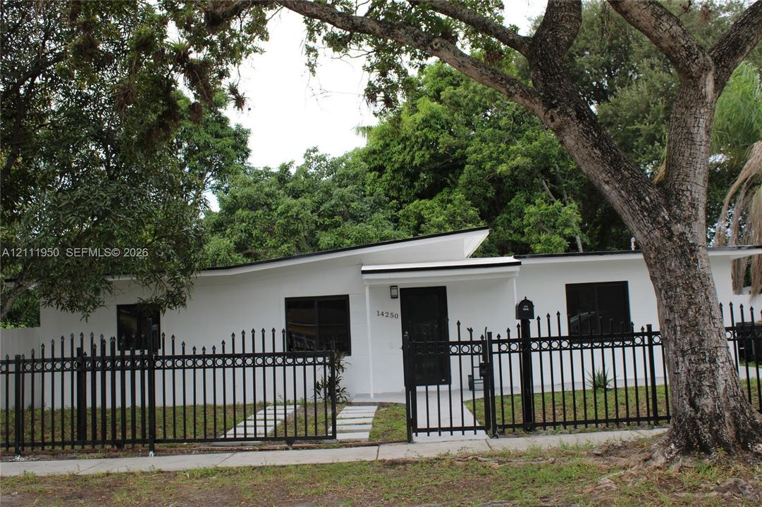 Single-story residence featuring a low-slope roofline, white exterior finish, dark-framed windows, and a black wrought-iron perimeter fence