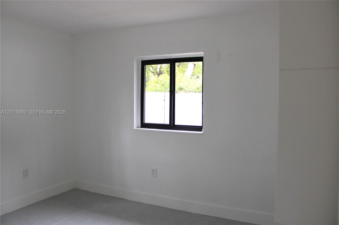 Neutral interior space featuring white walls, cool-toned tile flooring, and a single-hung window with a black frame