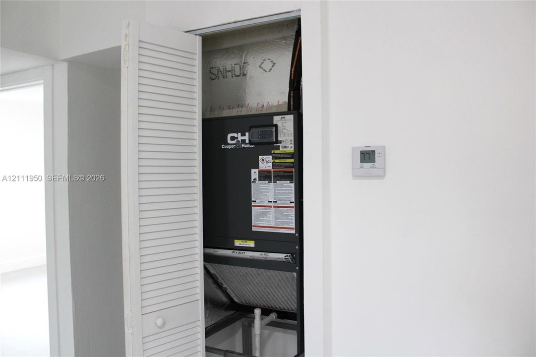 HVAC closet featuring a louvered bi-fold door, interior air handling unit, and wall-mounted digital thermostat