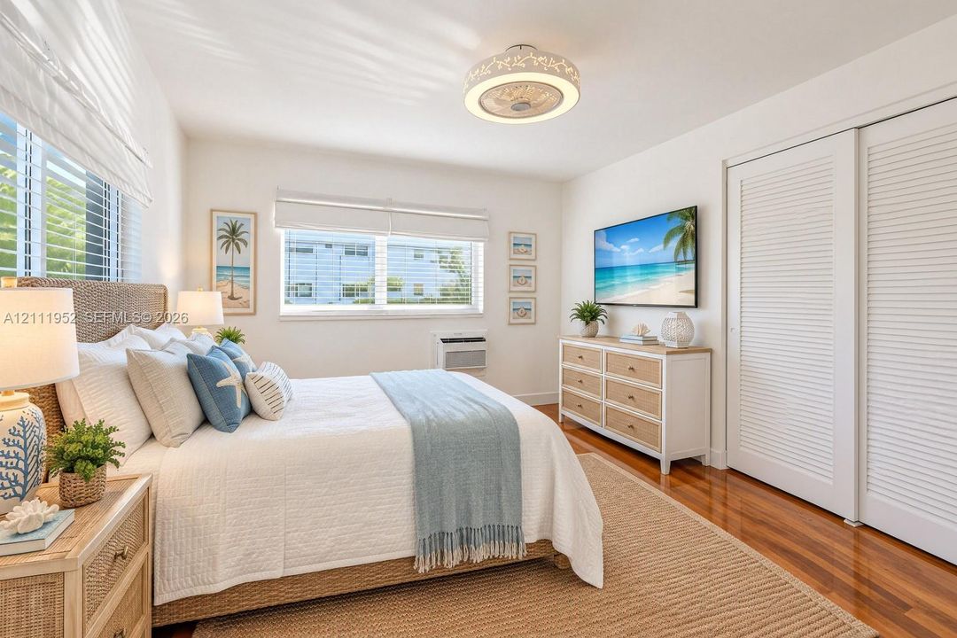 Wood flooring, white louvered sliding closet doors, impact windows with fitted roman shades, and a decorative circular LED lighting fixture with internal fan.