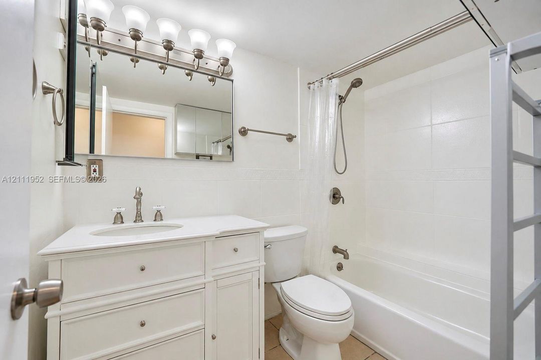 White vanity with a neutral countertop and integrated sink, chrome-finished multi-light fixture, mirror with a polished frame, and a tub-shower combination with tiled surround