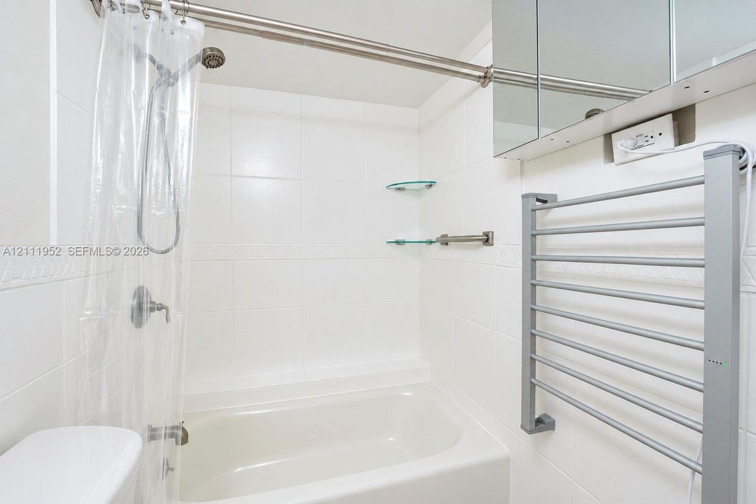 Full-size bathtub with white tile surround, wall-mounted metal heated towel rack, and mirrored medicine cabinet