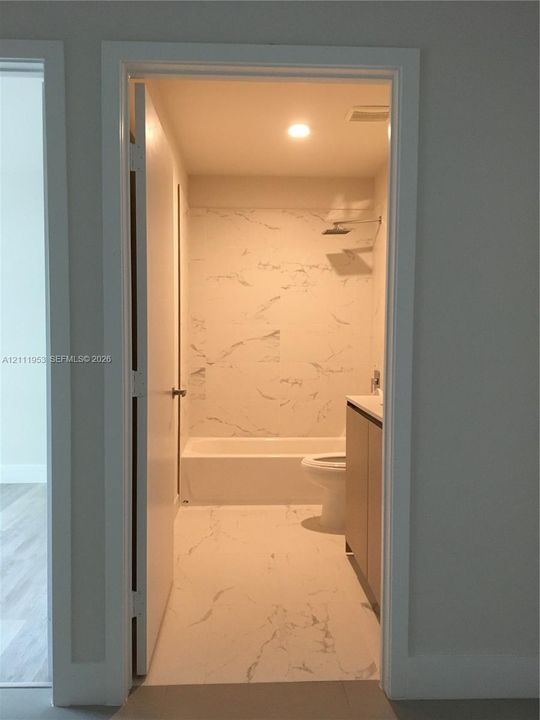 Bathroom featuring floor-to-ceiling stone-patterned wall tile, recessed ceiling lighting, a soaking tub, and a vanity with modern cabinetry