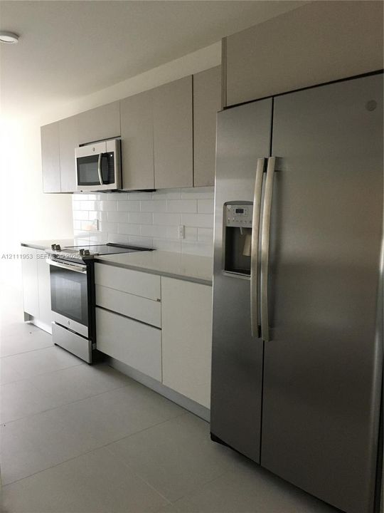 Kitchen featuring flat-panel cabinetry, stainless steel appliances, white subway tile backsplash, and light-toned solid surface countertops