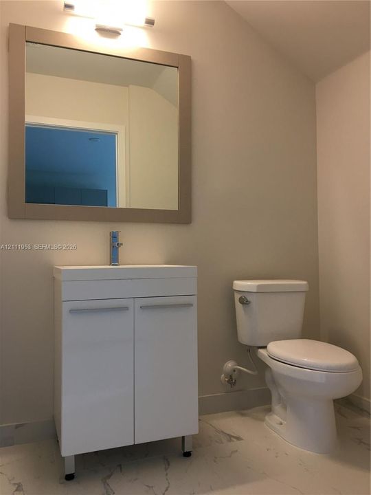 Glossy white vanity with a single-lever chrome faucet, rectangular wall-mounted mirror with a neutral frame, integrated light fixture, and stone-finish tile flooring