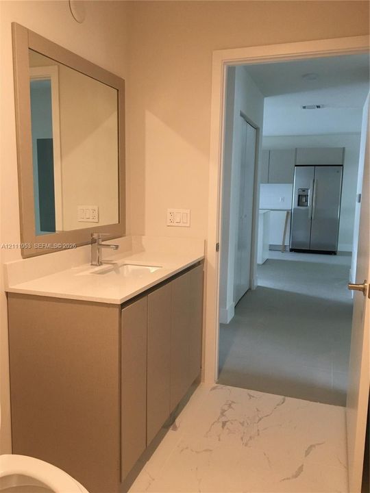 Vanity with neutral-tone cabinetry, rectangular undermount sink, solid-surface countertop, framed wall mirror, and chrome faucet hardware