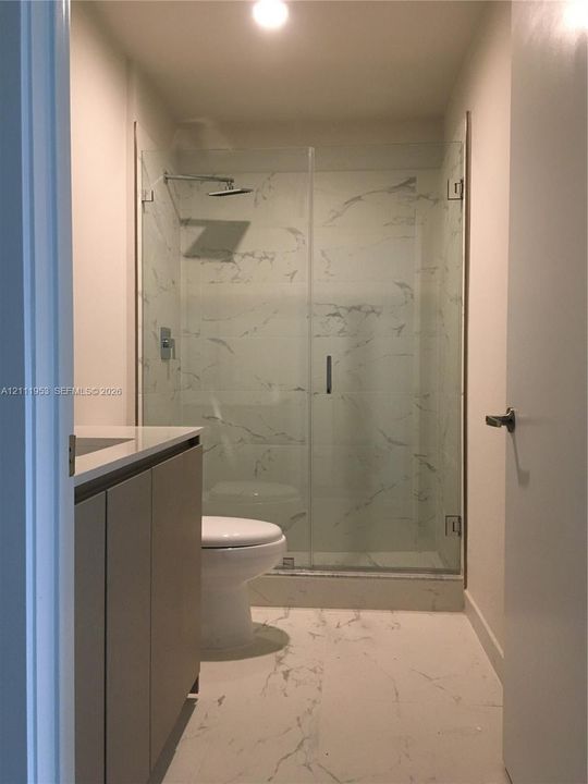 Bathroom featuring a glass-enclosed shower with floor-to-ceiling stone-pattern tile, a vanity with a solid-surface countertop, and stone-pattern floor tile