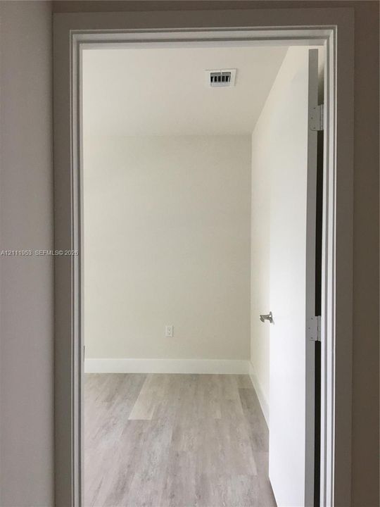 Neutral interior space featuring wood-finish flooring, crisp off-white wall finishes, and a classic door frame with a satin nickel lever handle