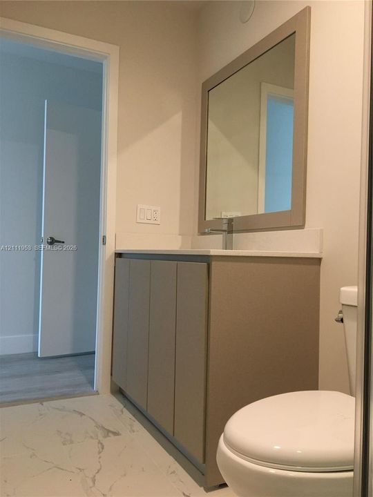 Bathroom vanity featuring a solid-surface countertop, rectangular undermount sink, integrated cabinetry, framed mirror, and marble-patterned tile flooring