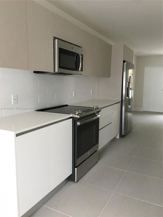 Contemporary kitchen featuring flat-panel cabinetry, stone countertops, a white subway tile backsplash, stainless steel appliances, and large-format floor tile