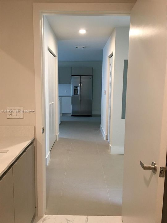 Large-format light tile flooring, neutral wall tones, recessed lighting, white louvered closet doors, and stainless steel refrigerator