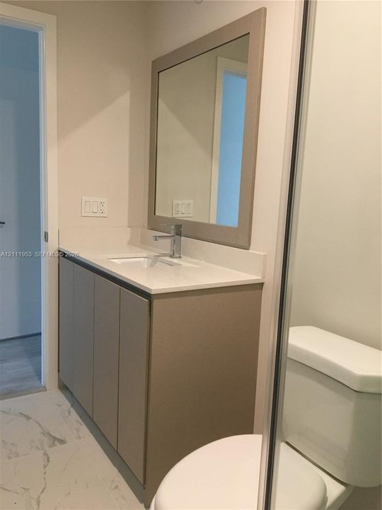 Vanity featuring flat-panel cabinetry, a light-toned stone countertop, an integrated rectangular sink, a chrome single-handle faucet, and a framed mirror