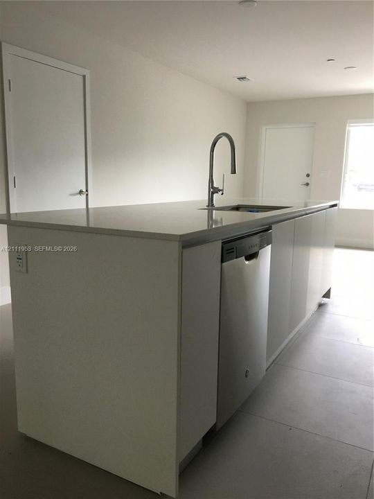 Kitchen island featuring solid-surface countertops, stainless steel undermount sink, high-arc pull-down faucet, and integrated stainless steel dishwasher