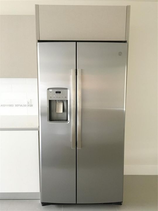 Stainless steel side-by-side refrigerator featuring an integrated water and ice dispenser, set within a custom cabinet surround