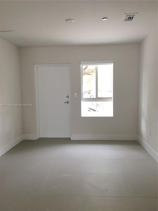 Neutral-toned room featuring large-format tile flooring, a solid core entry door, and a single-pane window