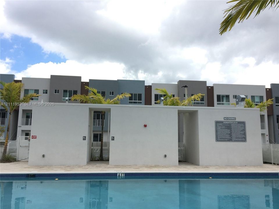 Swimming pool with tile edging and stone-paved deck, set against a multi-story exterior with stucco finish and palm landscaping