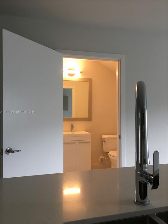 Modern kitchen featuring a stone-composite countertop with a polished chrome high-arc faucet, complemented by a white vanity, rectangular mirror, and wall-mounted light fixture