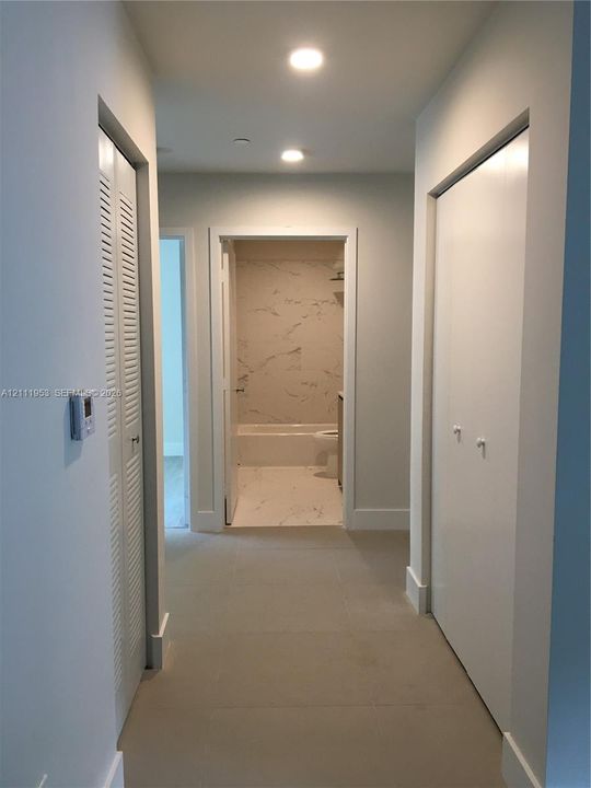 Hallway featuring neutral tile flooring, dual louvered and solid-panel closet doors, and recessed lighting