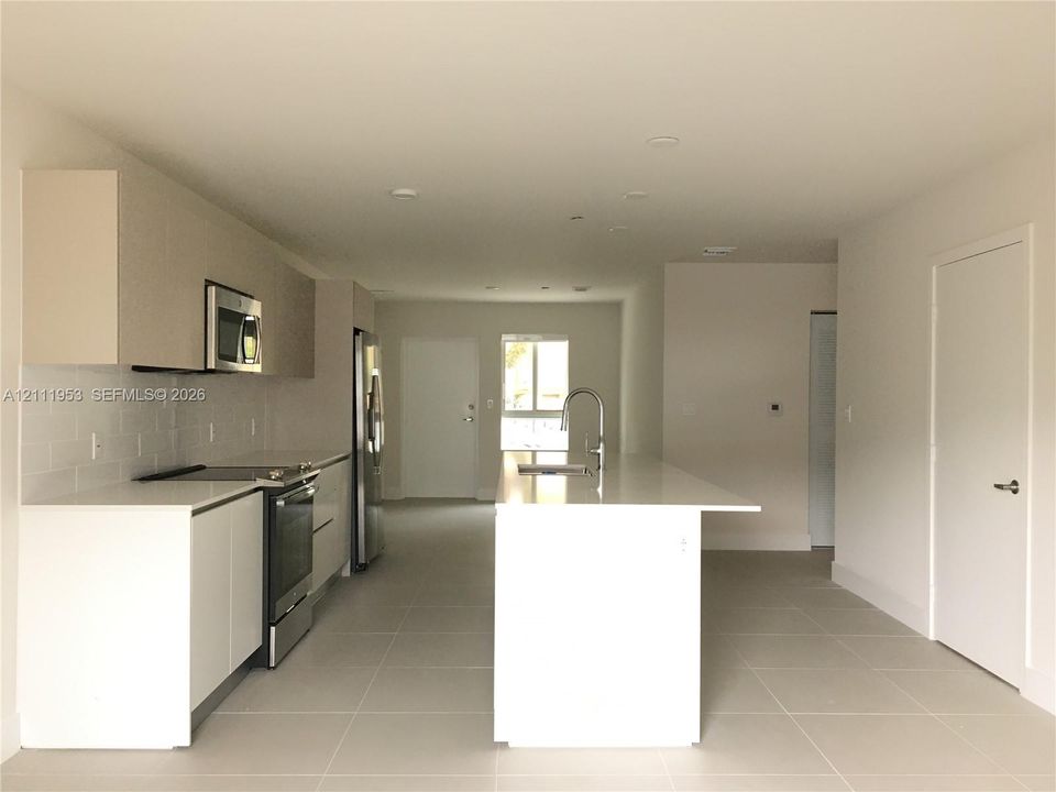 Kitchen featuring flat-panel cabinetry, quartz countertops, a central island with an integrated sink, stainless steel appliances, and subway tile backsplash