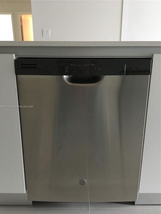 Stainless steel dishwasher with a top-mounted control panel, integrated between white cabinetry and topped with a solid surface countertop