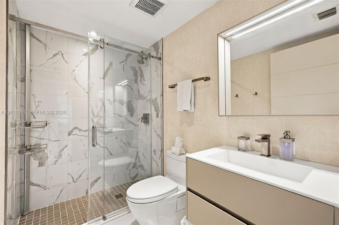 Floating vanity with integrated rectangular sink and metallic faucet, complemented by a walk-in shower featuring sliding glass doors and large-format veined tile surround
