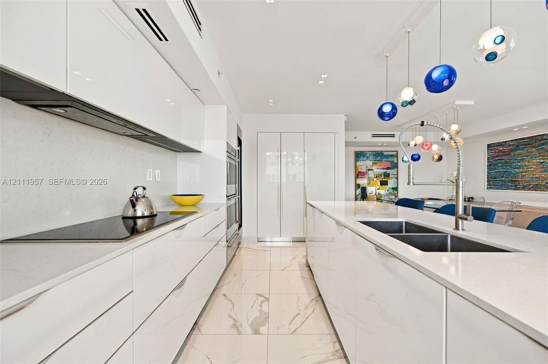 Contemporary kitchen featuring high-gloss cabinetry, quartz countertops, large-format veined tile flooring, a stainless steel double-basin sink with pull-down faucet, and built-in stainless steel double wall ovens