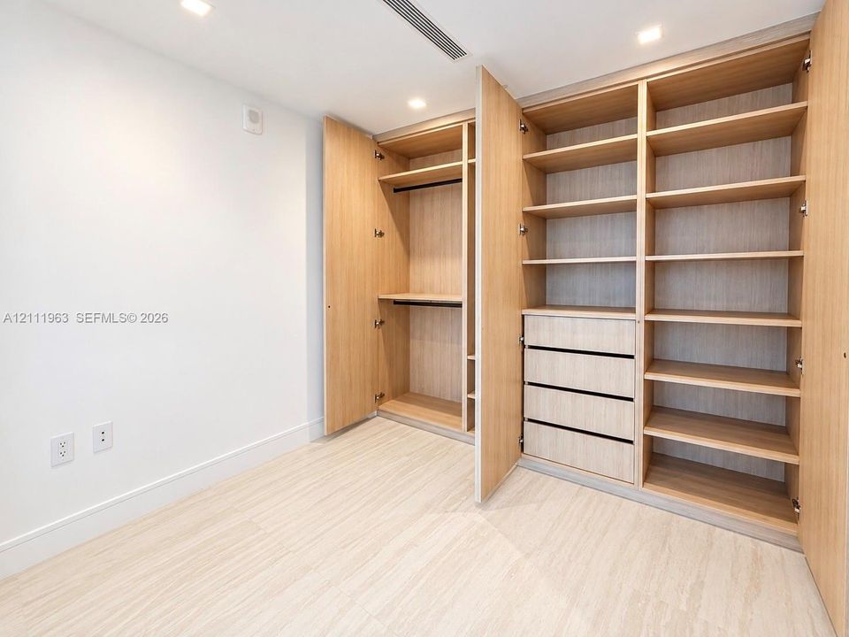 Custom built-in closet featuring light wood-finish cabinetry, adjustable shelving, integrated drawer storage, and recessed ceiling lighting