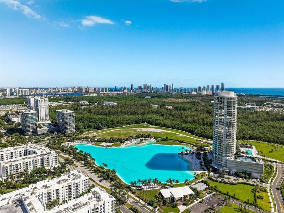 Aerial perspective featuring a large crystalline lagoon, coastal skyline, and dense woodland surroundings