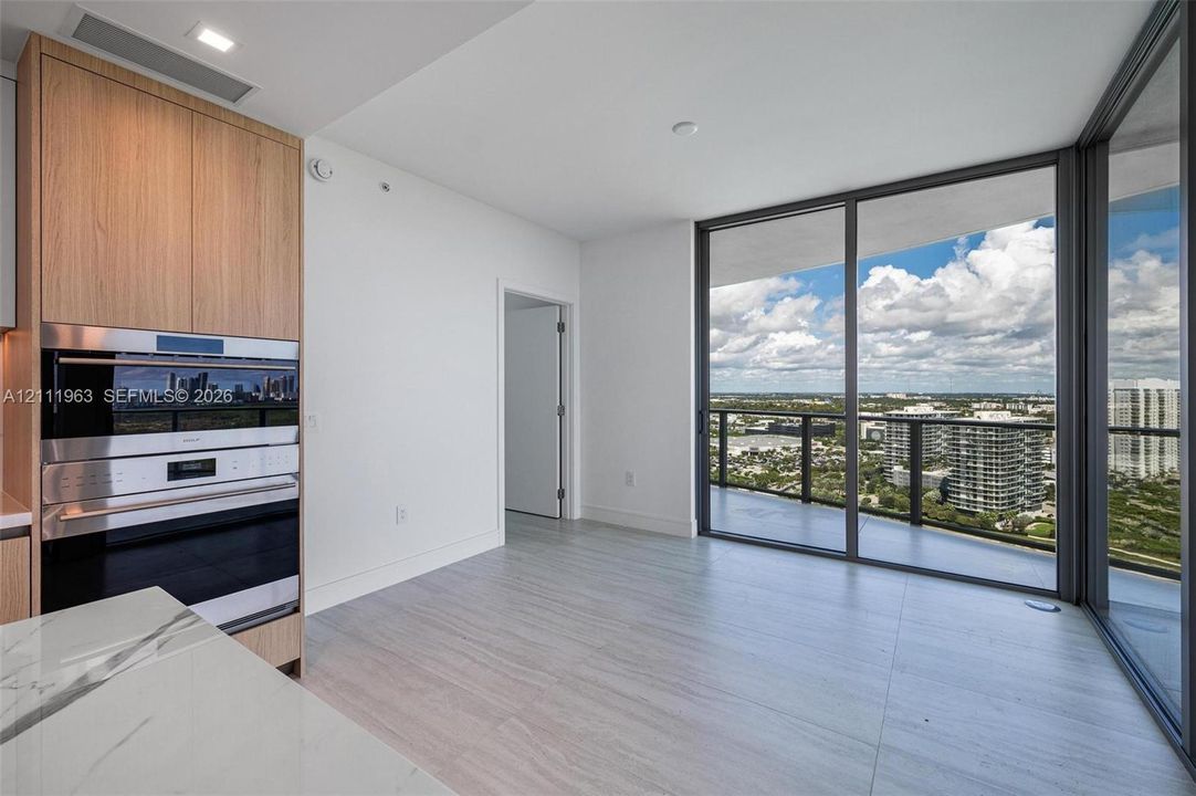 Floor-to-ceiling glass sliding doors, wood-finish cabinetry, built-in double wall oven, light-toned tile flooring, and stone-surfaced island