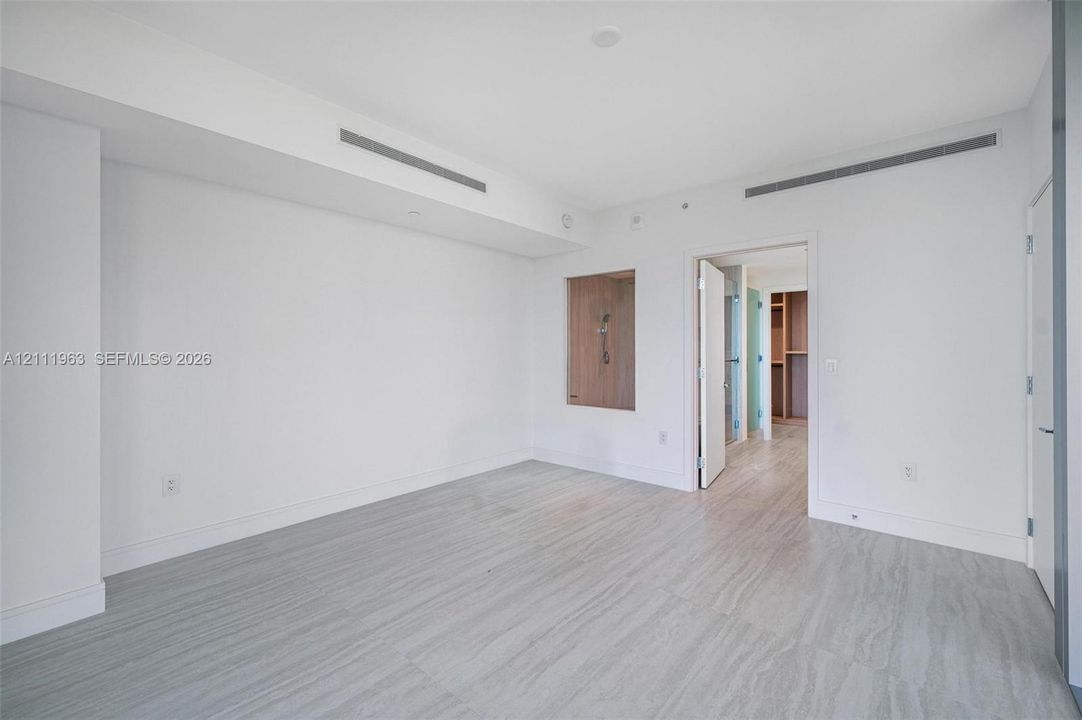 Neutral interior space featuring recessed linear ceiling diffusers, light-toned wood-finish flooring, a built-in recessed wall niche, and minimalist solid-core doors