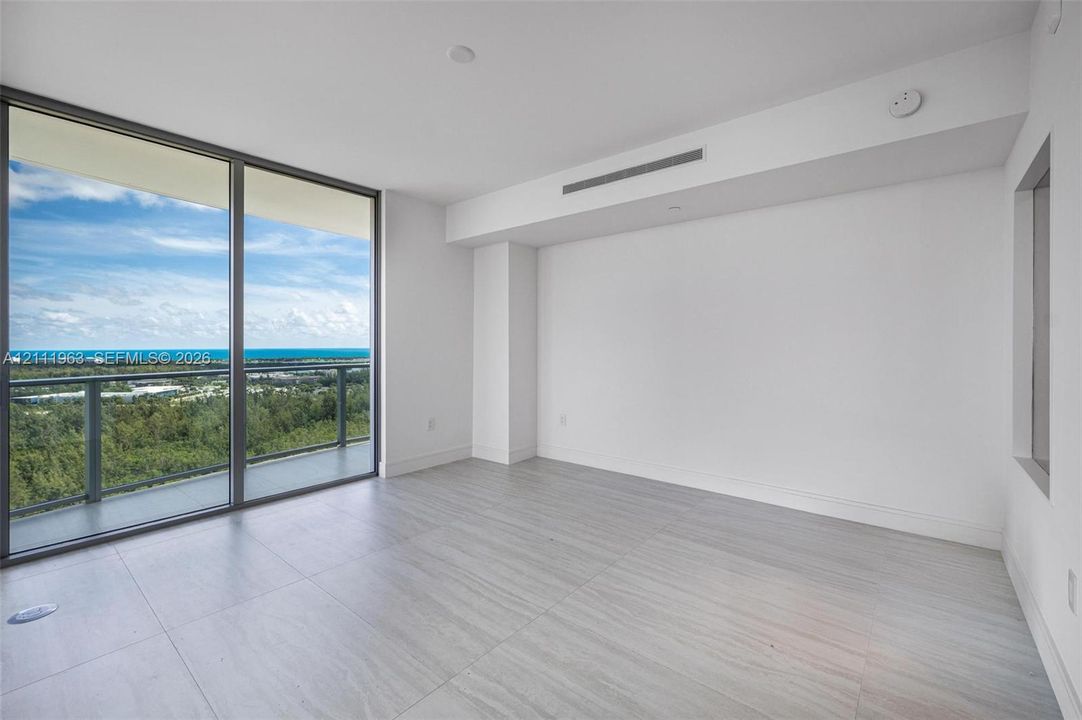 Floor-to-ceiling glass sliding doors, private balcony, neutral large-format tile flooring, and coastal landscape