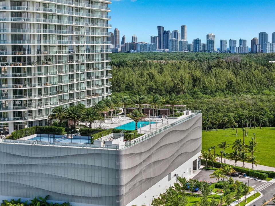 Elevated recreational deck featuring a swimming pool, tennis court, and lush landscaping