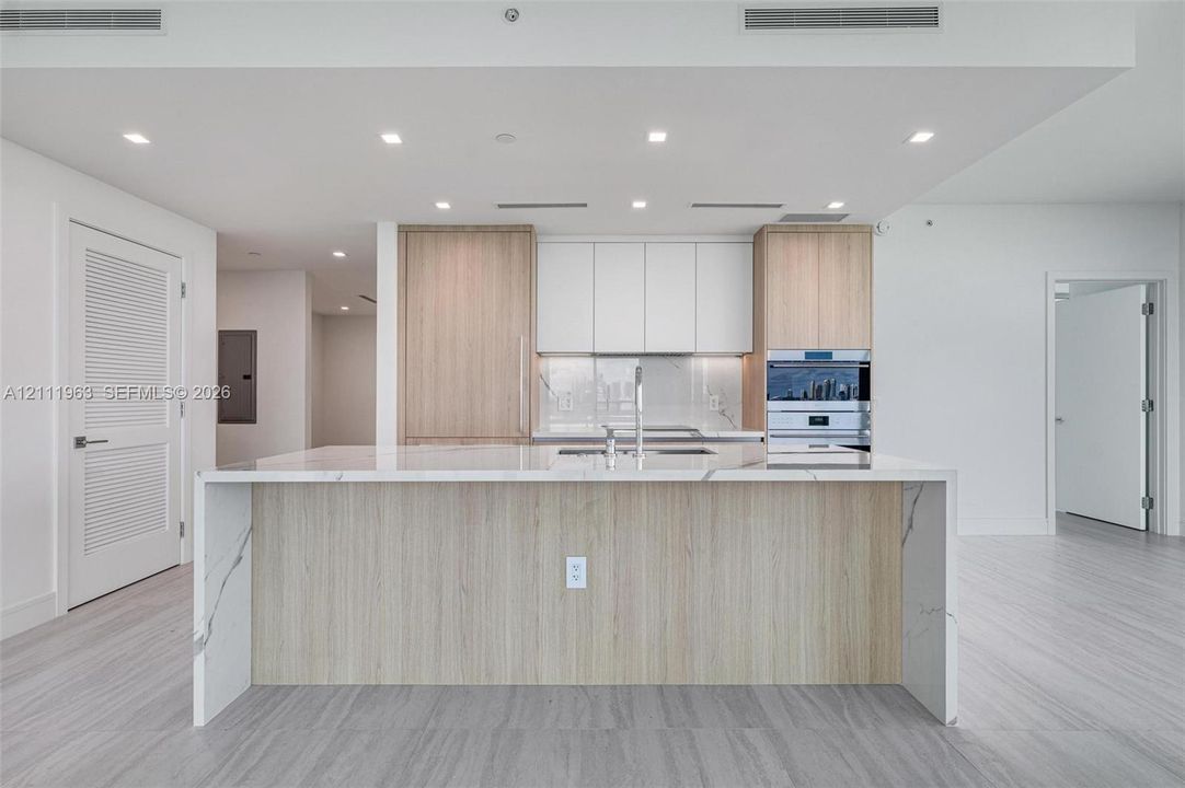 Kitchen featuring a waterfall island with a stone-finish countertop, wood-finish cabinetry, built-in double wall oven, and recessed lighting